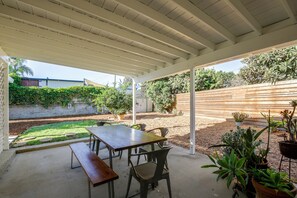 An outdoor patio with a table and benches, surrounded by potted plants and a wooden fence. - Pet-Friendly Central Home w/ Fenced Yard! (San Diego)