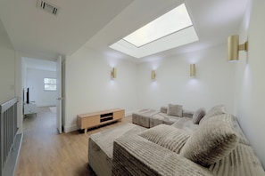 Ein modernes Wohnzimmer mit Oberlicht, einer Sofagarnitur, einer Holzunterhaltungseinheit und einem Fernseher.