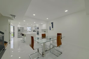 Eine moderne Küche mit weißen Schränken, Edelstahlgeräten und einem Glastisch mit Metallstühlen.