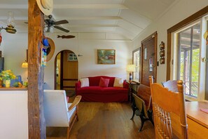 A cozy room with a red sofa, wooden furniture, a ceiling fan, and a painting on the wall. - Rustic Cabin-Stunning View-Cov Porch<br>Delaware Gem! (Damascus)