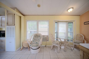 A room with a dining table, two wicker chairs, a small round table, and a television.