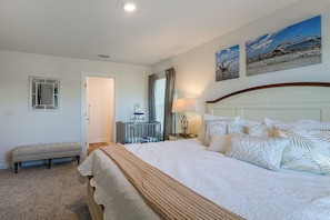 A hotel room with a large bed, a bedside table, a lamp, a crib, and two paintings on the wall. - 2 Mi to Panama City Beach: Modern Townhome (Panama City Beach)