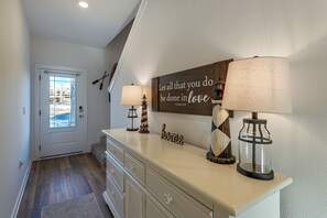 A hallway with a white door, a mirror, a wall-mounted sign with a biblical verse, and two table lamps with decorative bases. - 2 Mi to Panama City Beach: Modern Townhome (Panama City Beach)