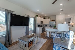 A modern kitchen with white cabinets, a flat-screen TV, and a dining area with bar stools. - 2 Mi to Panama City Beach: Modern Townhome (Panama City Beach)