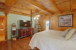 Een kamer met houten lambrisering, een bed, een dressoir, een televisie en een schilderij aan de muur.