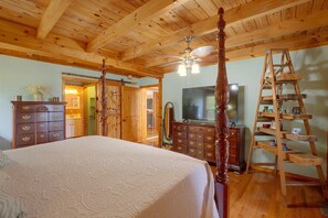 Ein Schlafzimmer mit einem großen Bett, Holzbalkendecke, einem Chandelier, einem Schmuckkästchen, einem Fernseher und einer Holzleiter.