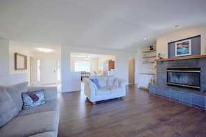 A spacious living room with a fireplace, a sofa, and a dining area in the background. - Helena Valley Home w/ Mtn Views & Acre (Clancy)