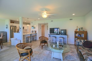 A living room with a glass coffee table, wicker chairs, a television, and a bookshelf. - Aransas Bayfront,  Fishing Pier and Boat Ramp (Rockport)