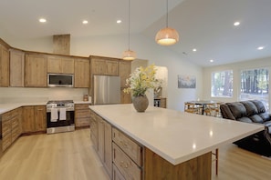 A modern kitchen with wooden cabinets, stainless steel appliances, a large island, and a dining area with a view. - Bring Your Boat! Home w/ Patio Near Lake Almanor (Chester)