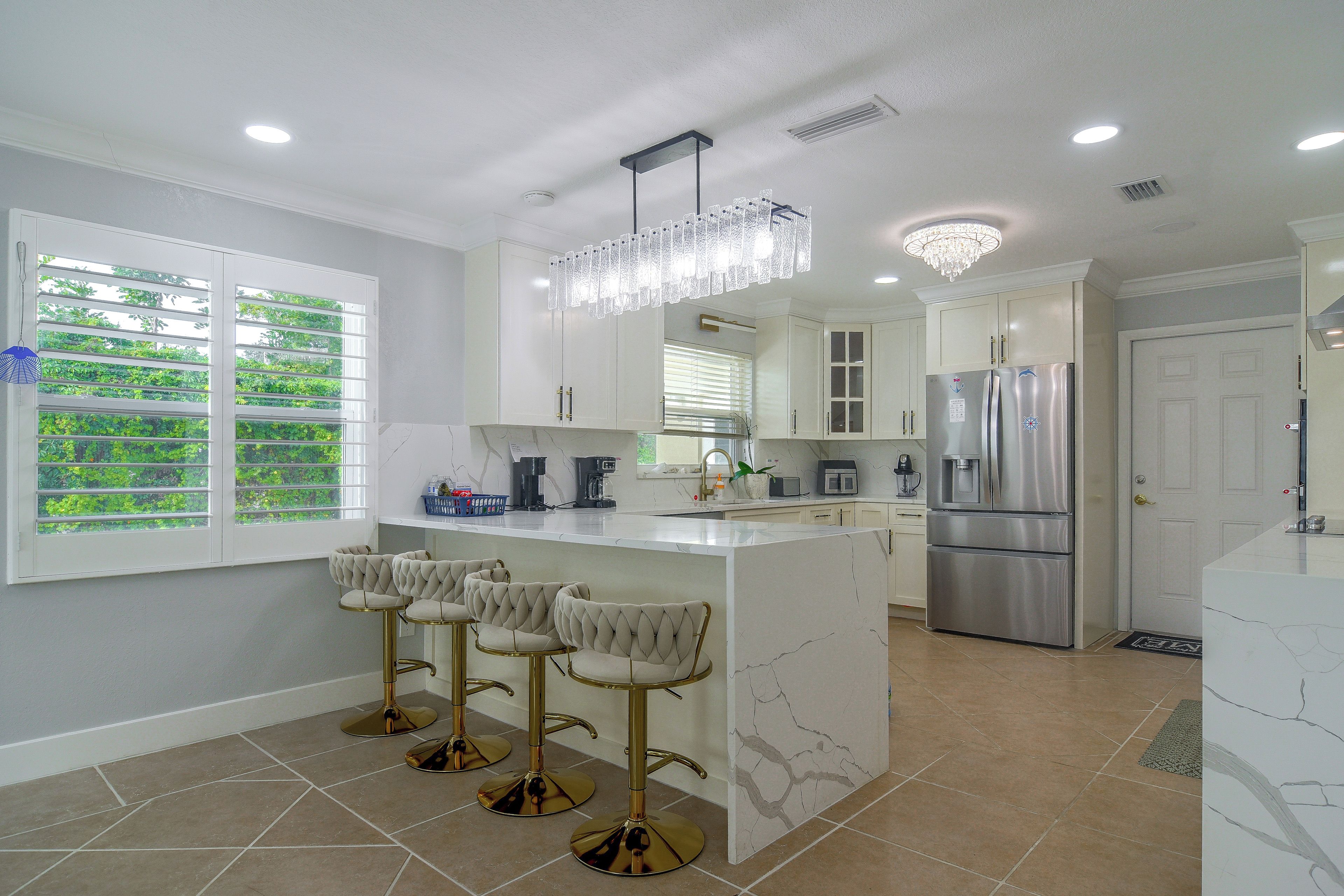 A modern kitchen with a marble island, stainless steel appliances, and a chandelier.
