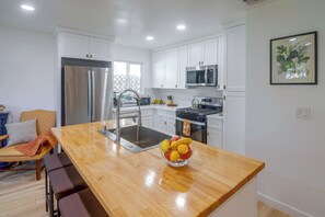 A modern kitchen with white cabinetry, stainless steel appliances, and a wooden island with a fruit bowl. - North Hollywood Home, Extended Stay (Los Angeles)