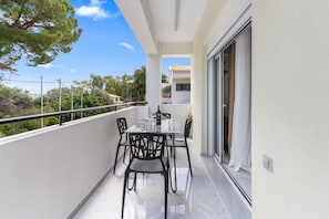 Ein Balkon mit einem Glastisch und Stühlen, einer Flasche und einem Weinglas.