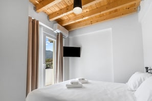 Ein Schlafzimmer mit einem Bett, einem Flachbildfernseher an der Wand und einem Fenster mit Vorhängen.