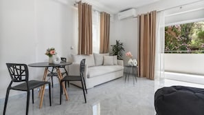 Ein modernes Wohnzimmer mit einer Couch, einem Esstisch mit Stühlen und einem Balkon mit Vorhängen.