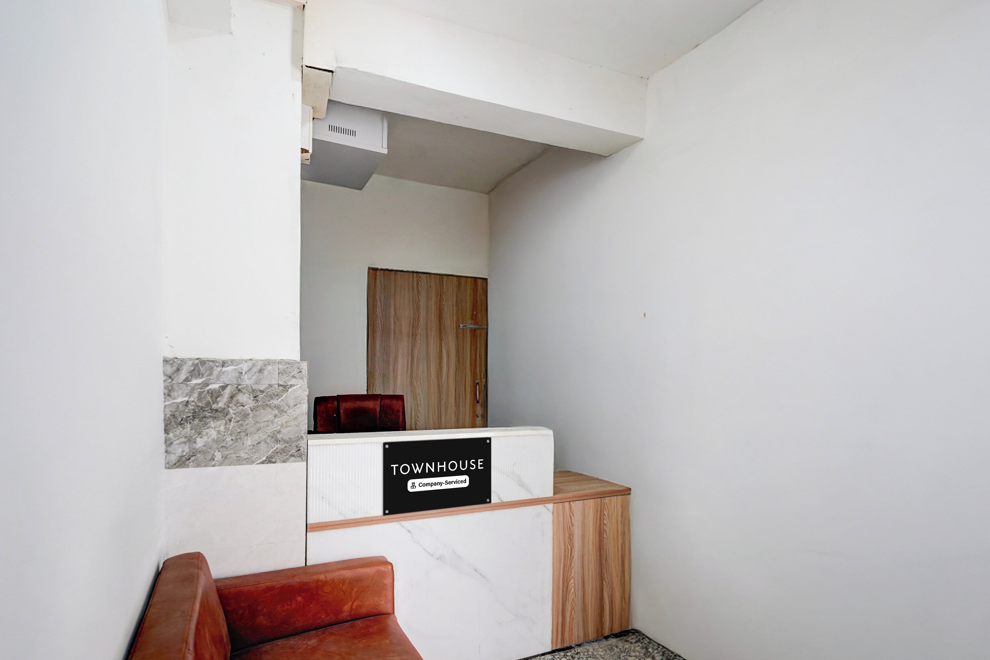 Zona de recepción de un hotel con pared de mármol, un armario de madera y un sillón de cuero rojo.