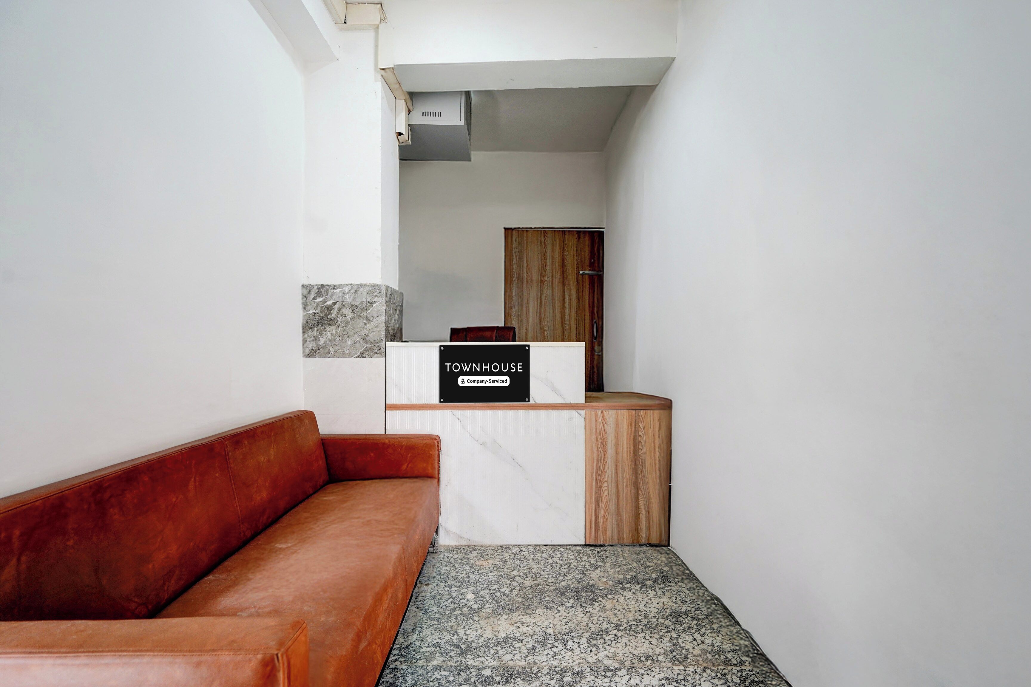 A reception area with a marble counter, a wooden cabinet, and a red leather couch.