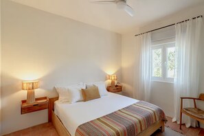 A bedroom with a bed, two bedside tables with lamps, a chair, and a window with curtains. - Monte do Areal (Santiago do cacem)