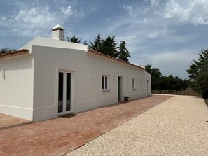 A single-story building with a flat roof, a chimney, and a gravel driveway. - Monte do Areal (Santiago do cacem)