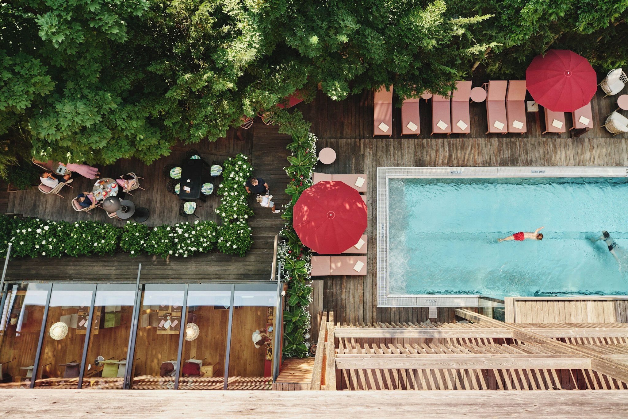 Un espace piscine extérieur doté de chaises longues et de parasols, entouré de verdure et d’une terrasse en bois.