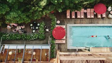 Un espace piscine extérieur doté de chaises longues et de parasols, entouré de verdure et d’une terrasse en bois.