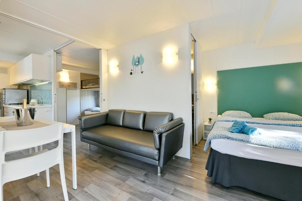 Una habitación de hotel moderna con sofá, cama, una mesita y una kitchenette.