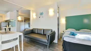 Una habitación de hotel moderna con sofá, cama, una mesita y una kitchenette.