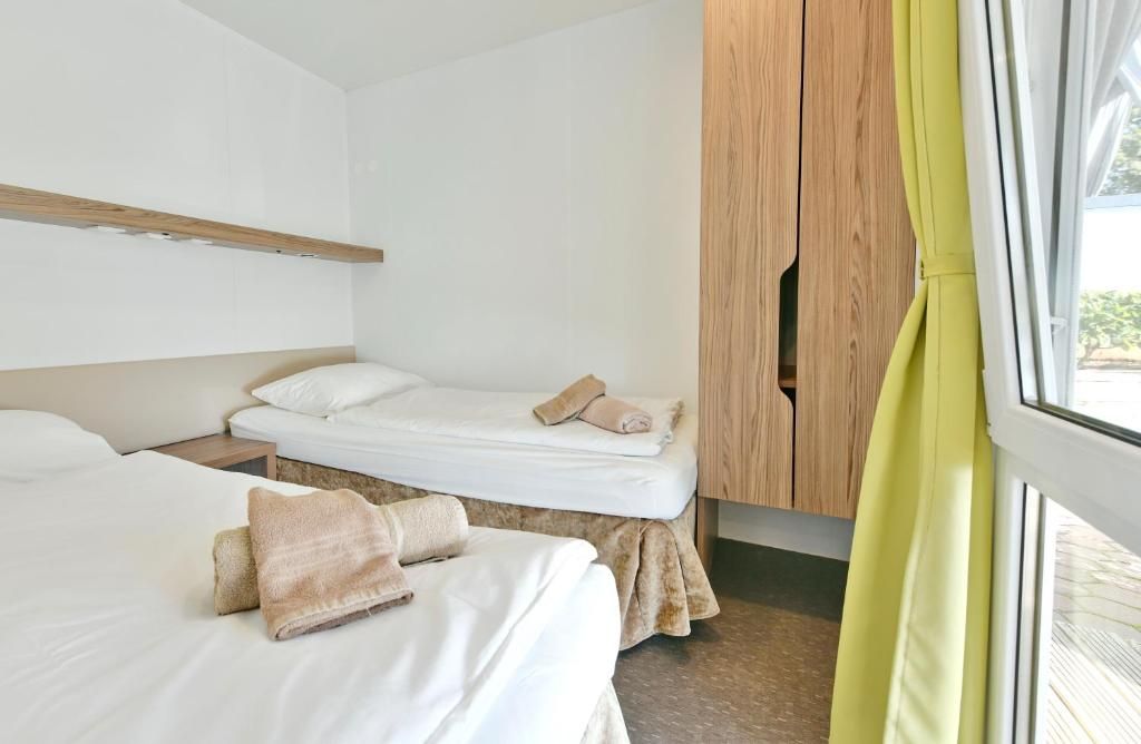 A hotel room with two beds, a wooden wardrobe, and a window with curtains.