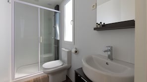 A modern bathroom with a glass-enclosed shower, a toilet, and a sink with a mirror above. - Polidor Camping Resort (FUNTANA)