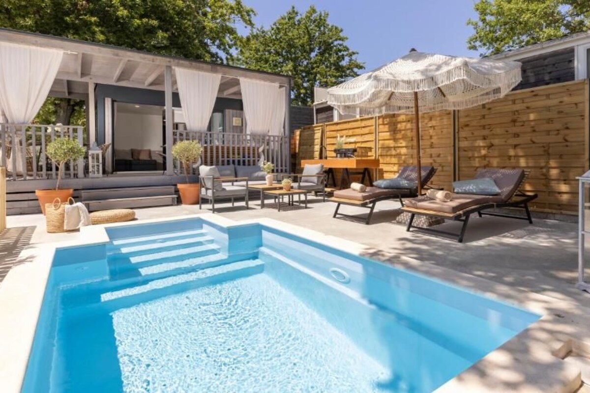 A swimming pool with lounge chairs and umbrellas, surrounded by wooden decking and a covered seating area.