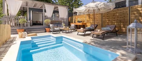 A swimming pool with lounge chairs and umbrellas, surrounded by wooden decking and a covered seating area.