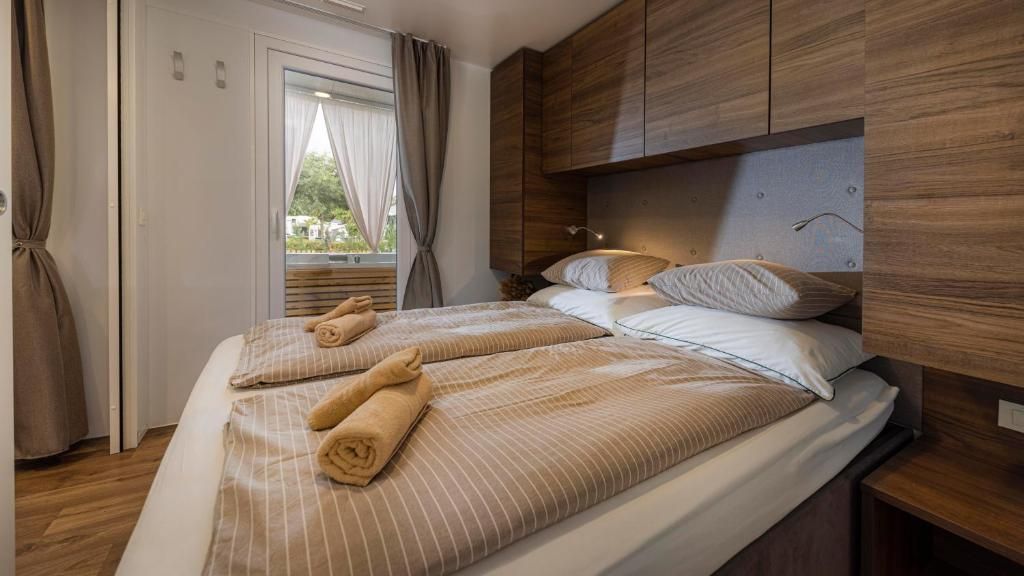 A hotel room with a bed, a nightstand, a window with curtains, and wooden paneling.