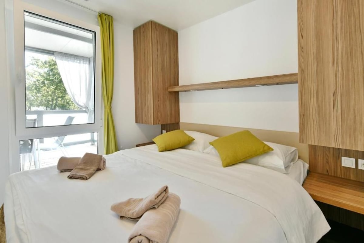 A hotel room with a bed, pillows, a window with curtains, and a wooden headboard.