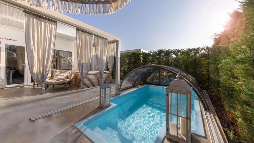 A modern outdoor swimming pool with a glass enclosure, a hanging chair, and a covered seating area.
