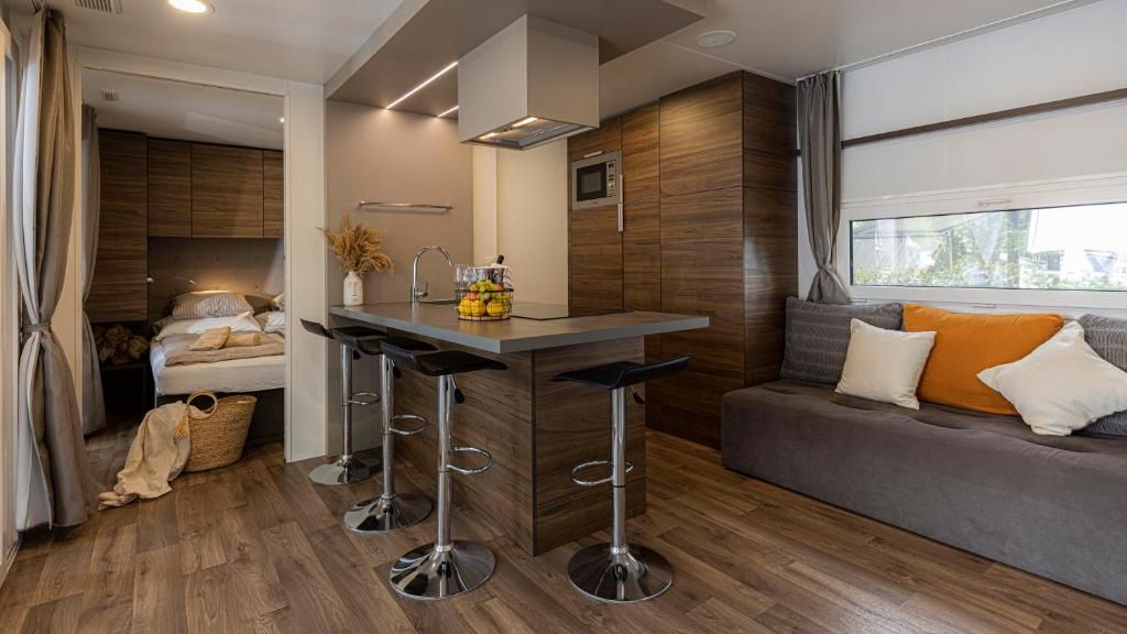 Un espacio habitable compacto con kitchenette, un sofá con cojines, una zona de comedor con taburetes y un ventanal que proporciona luz natural.