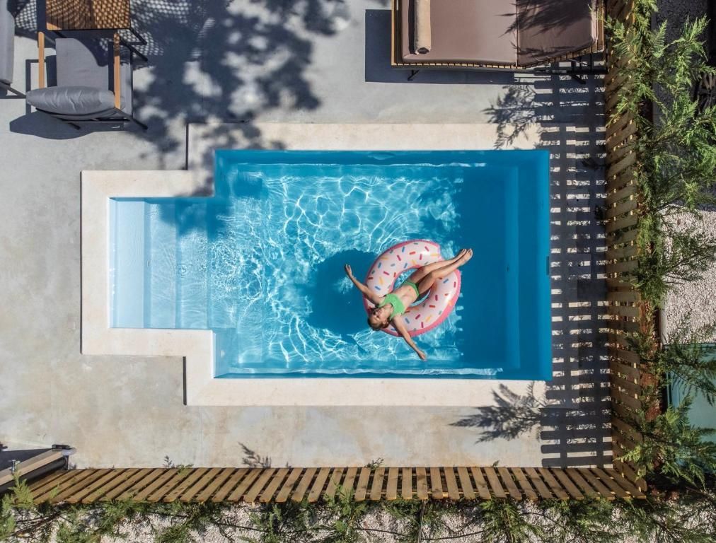 Vista aérea de una piscina con una persona en un flotador, rodeada por una terraza de madera y follaje.