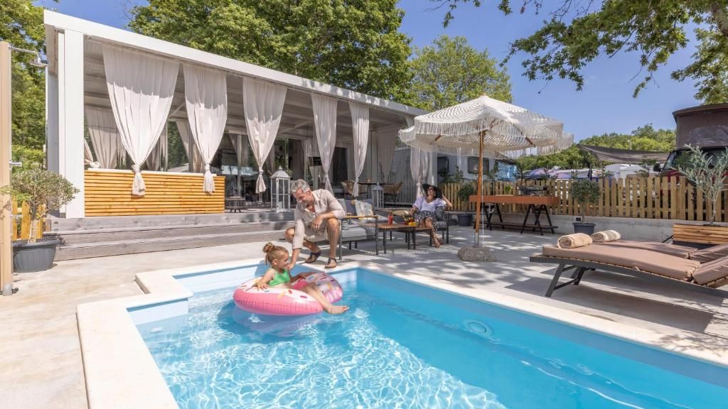 Een zwembadgedeelte met een overdekte zithoek, ligbedden en een houten terras.