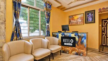 A hotel reception area with a reception desk, a seating area with chairs, and a painting on the wall.