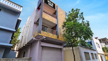 A modern hotel building with a prominent sign, a balcony, and a tree in front.