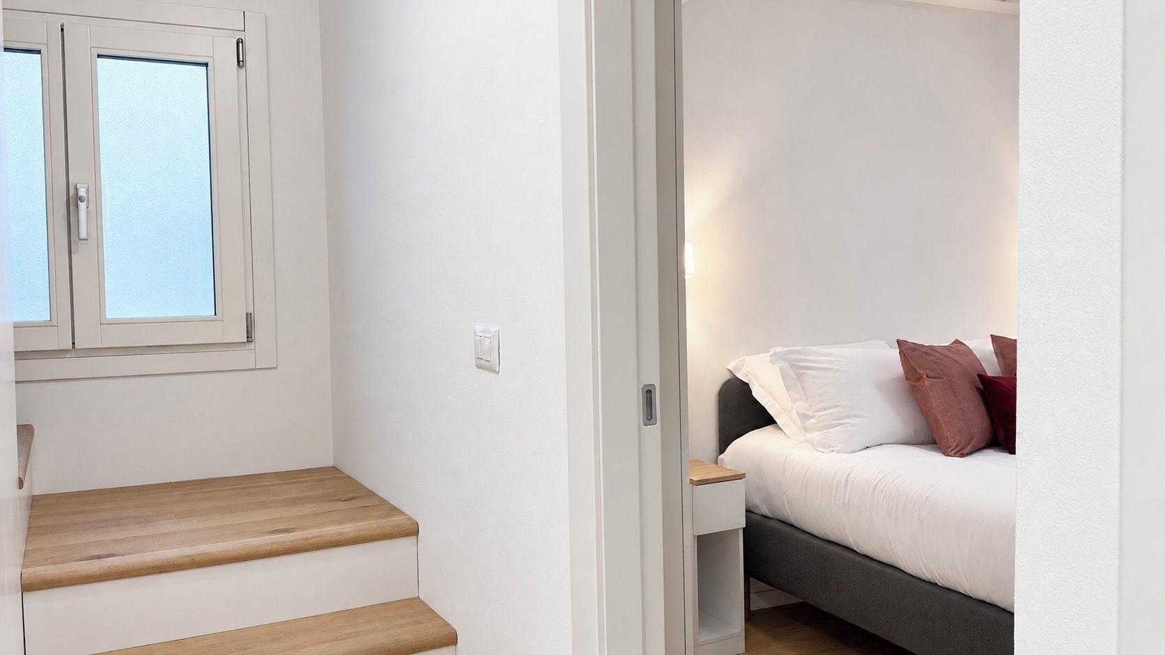 Un dormitorio con cama, almohadas, mesita de noche y banco de madera.