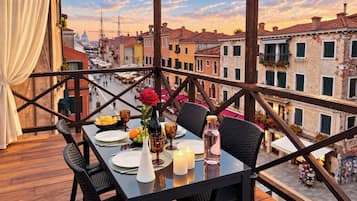 Un área de comedor al aire libre con una mesa dispuesta para dos, con vista a una calle con edificios históricos.