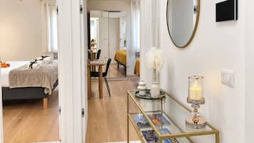Una habitación de hotel con cama, escritorio, espejo, mesita de noche con una vela y una mesa de centro de vidrio con revistas.