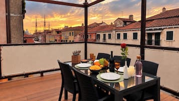 Mesa de comedor en un balcón con vista a edificios históricos y un atardecer.