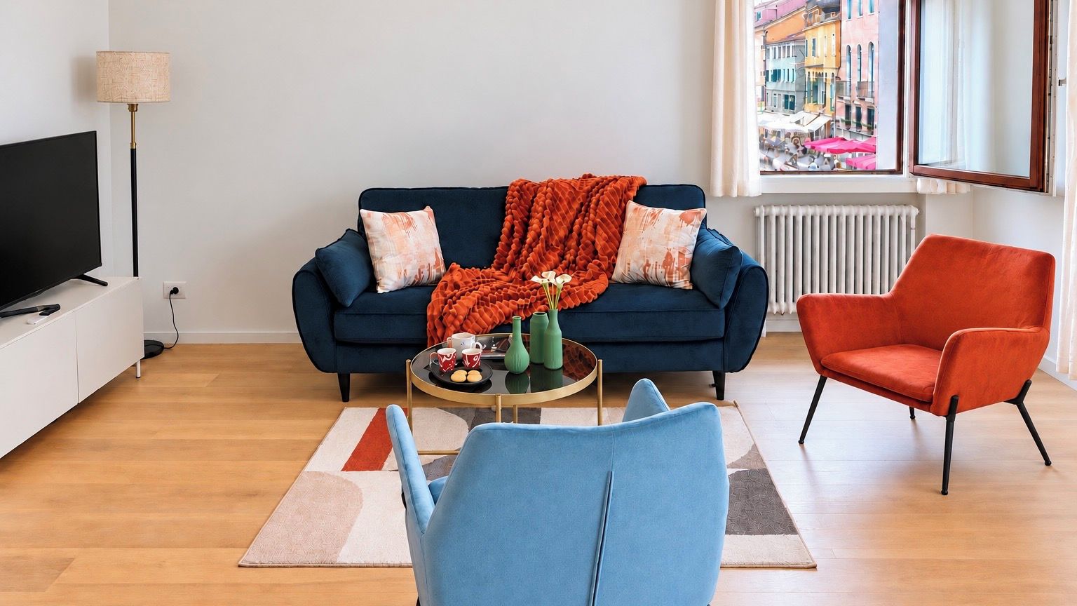 Una sala de estar moderna con sofá, una mesa de centro, televisor y vistas a un paisaje urbano a través de una ventana.