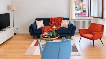 Una sala de estar moderna con sofá, una mesa de centro, televisor y vistas a un paisaje urbano a través de una ventana.