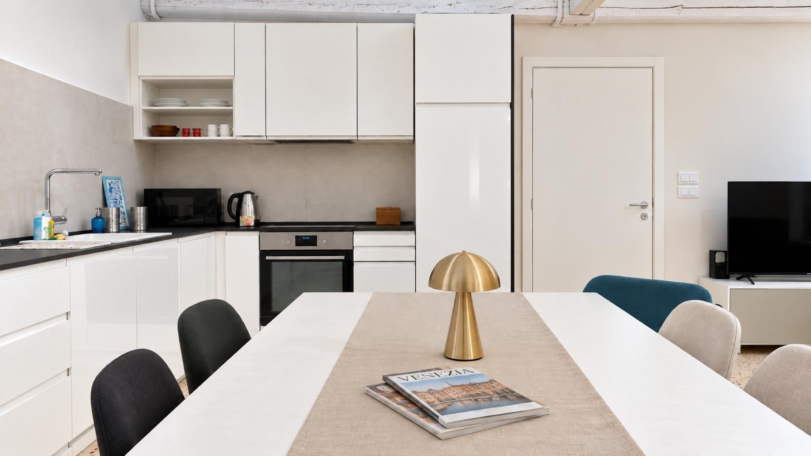 A modern kitchen with white cabinets, a built-in oven, and a dining area with a white table and chairs.