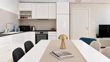 A modern kitchen with white cabinets, a built-in oven, and a dining area with a white table and chairs.