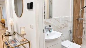 Un baño moderno con cabina de ducha de vidrio, lavamanos blanco con salpicadero de mármol y tocador con superficie de vidrio.