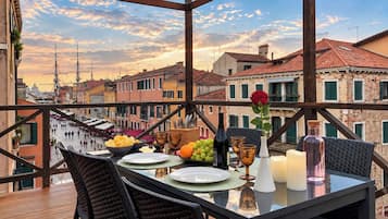 Un área de comedor al aire libre con una mesa preparada para dos, con vistas a un paisaje urbano con edificios históricos.