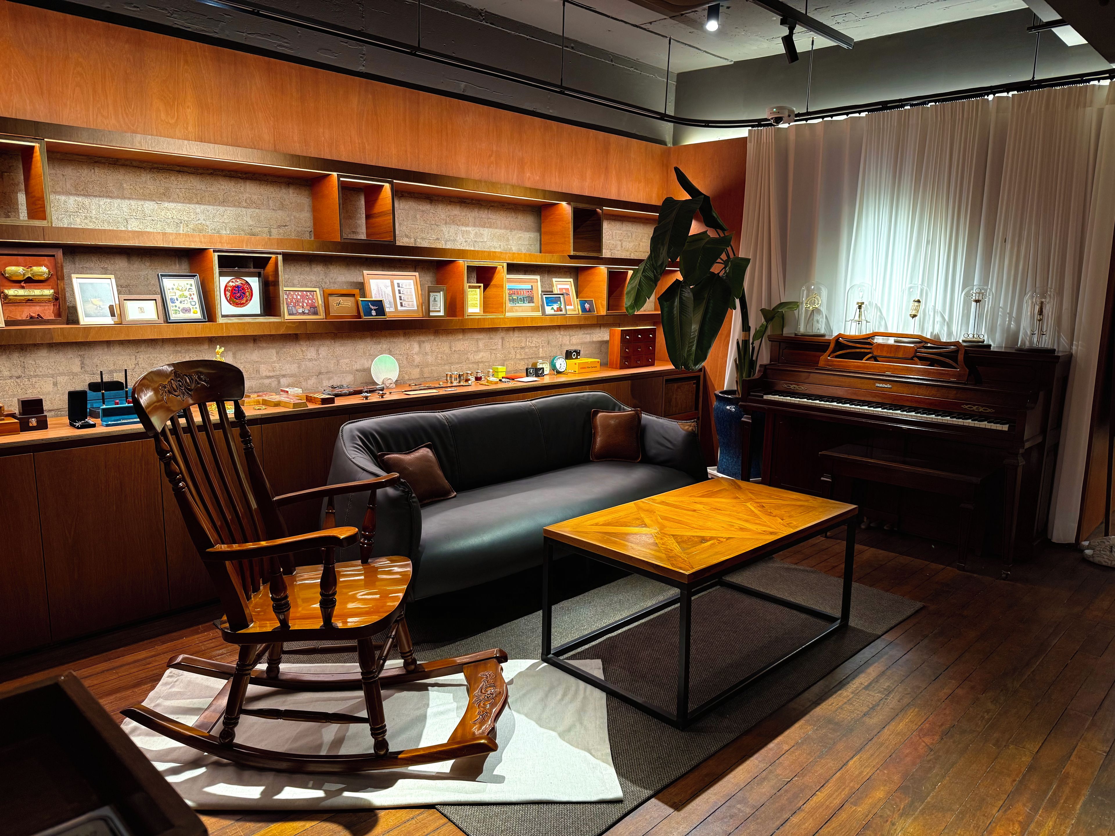Una sala acogedora con un sofá de madera, una mecedora, un piano y una estantería llena de fotografías enmarcadas.