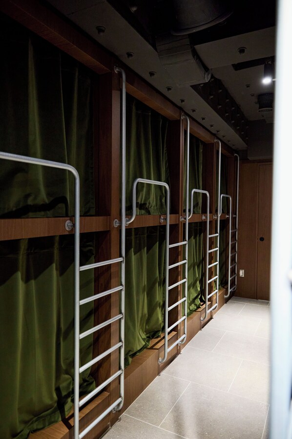 Un pasillo con literas, paredes de madera y cortinas verdes.